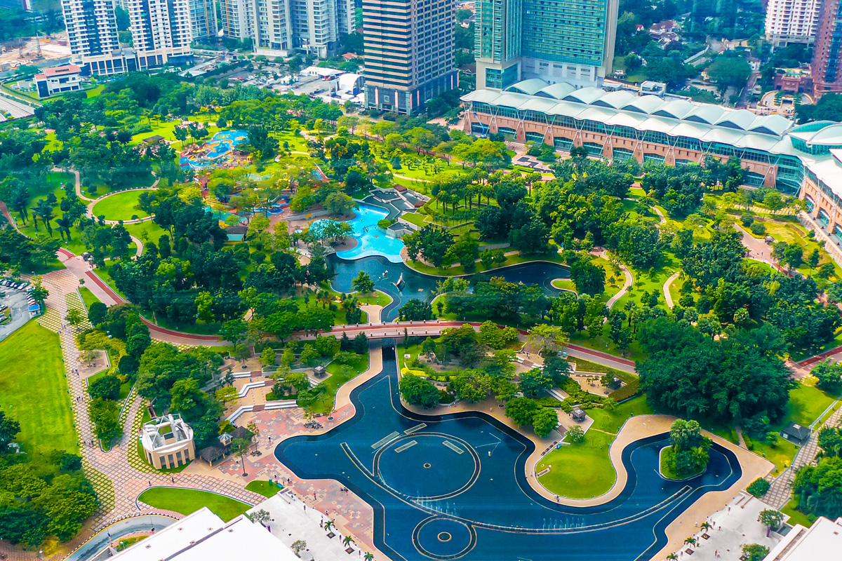 Aerial view of a vibrant urban park with lakes, walking paths, and modern skyline, showcasing lush greenery at The Heart of the City